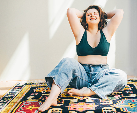 Chica sentada en una alfombra con los brazos levantados